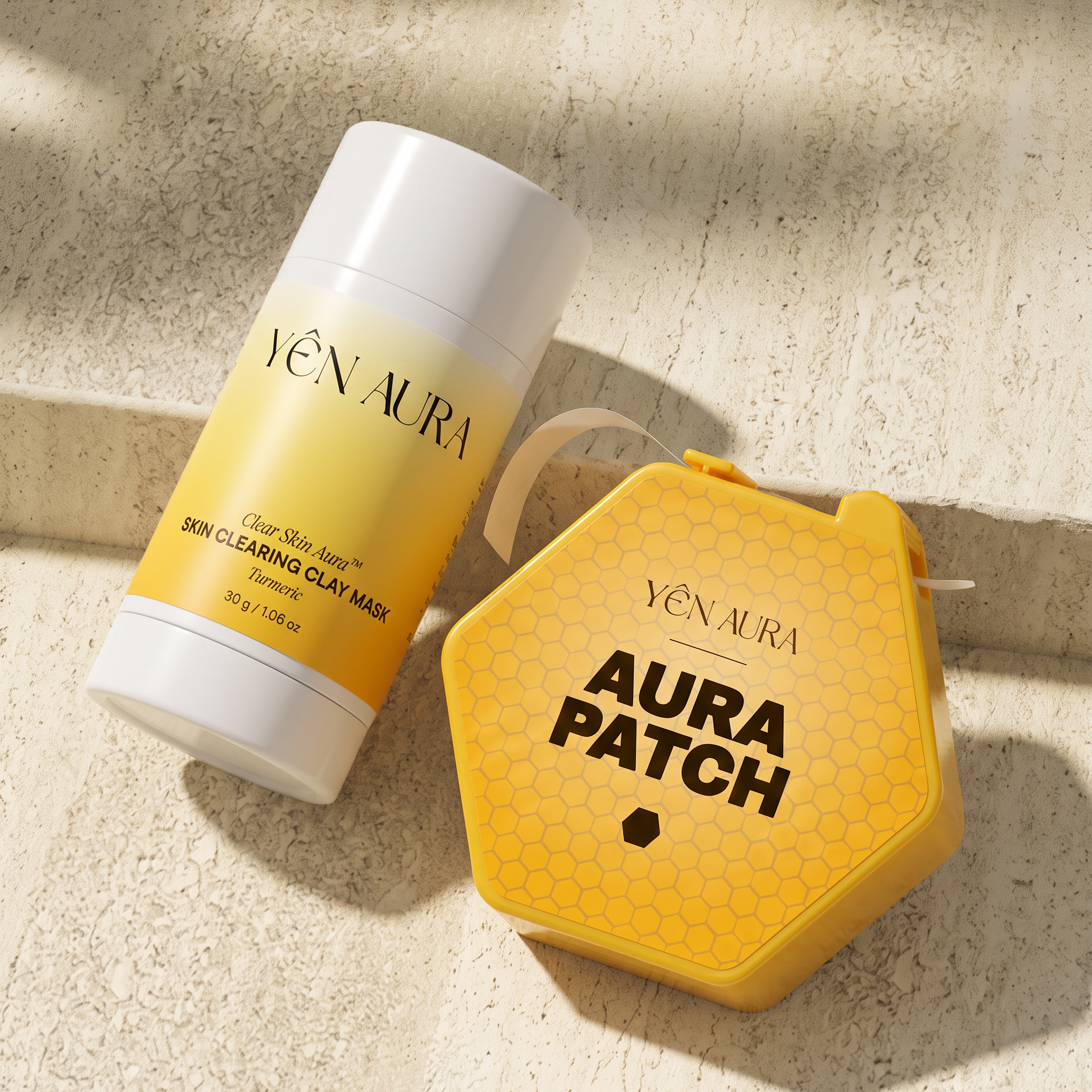 Yen Aura skincare products arranged on a textured beige stone surface: a yellow and white 'Skin Cleansing Clay Mask' stick and a yellow honeycomb-shaped 'Aura Patch' case with a white loop.